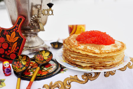 Pancakes with red caviar on the background of samovar and wooden dishes in Khokhloma style. Pancake week, snow, Russia.の写真素材