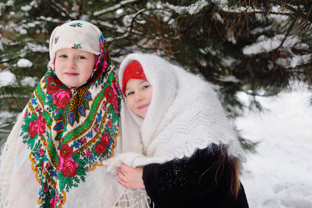 two little girls in fur coats and Russian scarves on the background of snow-covered treesの写真素材