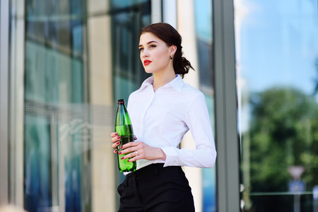 a cute young girl in business clothes on the background of an office building is holding a bottle of water.の写真素材