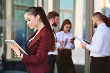 cute young businesswoman with computer tablet in hands on the background of office and colleagues on office workの写真素材