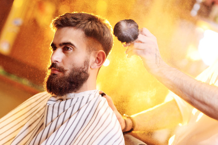 barber does a haircut for a young handsome man with a beard and mustache on the background of Barbashopの写真素材