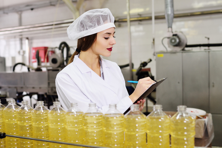 line of food production of refined sunflower oil. Girl worker at a factory on a conveyor background with bottles of vegetable oil.の写真素材