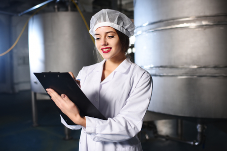 a pretty young girl scientist or worker in white uniform makes notes on paper against the background...