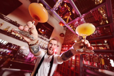 attractive young bartender smiling and giving the client a cocktail of orange colorの写真素材