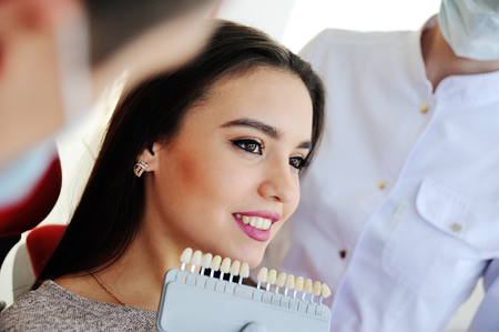 dentist and assistant pick up the color of teeth for a young girl patient. teeth whitening, tooth fillingsの写真素材