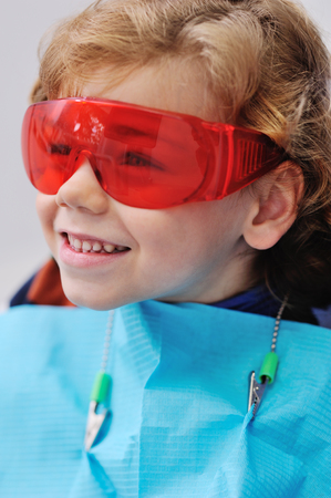 cheerful child boy with curly red hair in blue dental chair smilingの写真素材