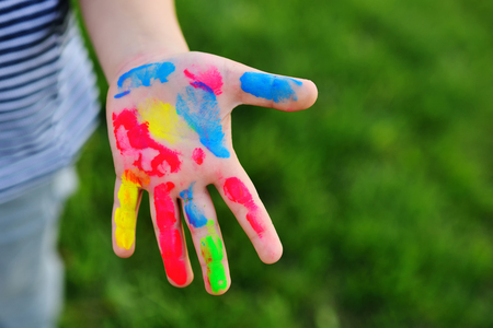 a childs hand is soiled in multicolored finger paints close-up on a grass background.copy spaceの写真素材
