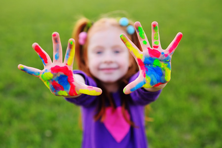 cheerful little girl with red hair shows her hands dirty with multicolored paints and smilesの写真素材
