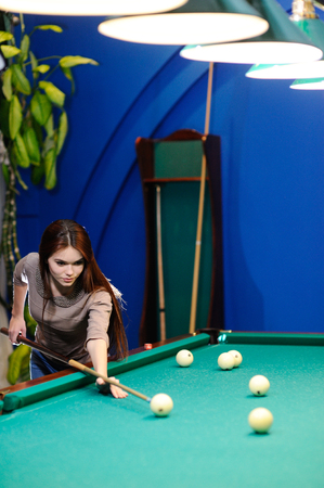 nice cute girl with a cue in her hands playing billiards
