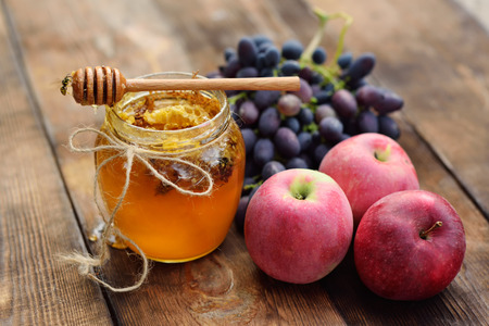 The wasps fly around the jar with honey, grapes and apples on a wooden backgroundの写真素材