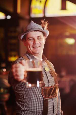 man in traditional Bavarian clothing at the Oktoberfest with a beer in hand smiles on the background of the pubの写真素材
