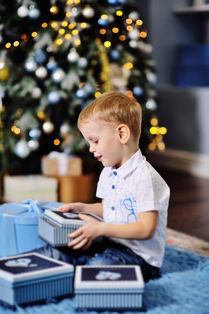 baby boy opens boxes with gifts under the Christmas tree and smilesの写真素材