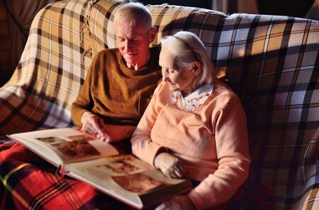 two elderly people-a man and a woman looking at a family photo album smile and hug each other...