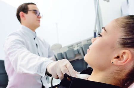 a doctor in a modern diagnostic clinic examines the thyroid gland of a patient of a young attractive woman on an ultrasound machine. Prevention of thyroid cancer.の写真素材
