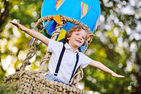 a child a small boy with curly hair in a basket of a blue balloon smilesの写真素材