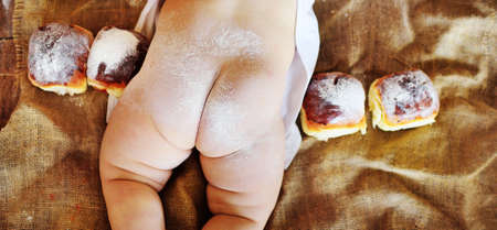 naked baby ass close up sprinkled with flour on the background of delicious muffins