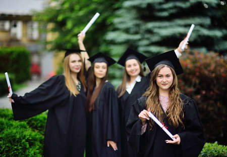 young girl, a university graduate student in a black robe and a square hat with a diploma in her...