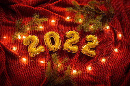 numbers 2022 on the background of a red knitted cozy plaid, Christmas tree branches and Christmas lights.の写真素材