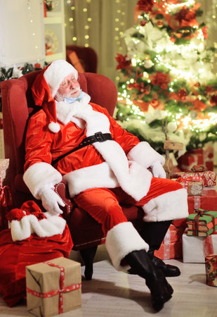 Tired Santa Claus is sitting on a chair with his medical mask off to take a deep breath of air.の写真素材