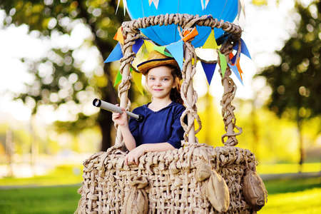 a cute little girl in a straw hat is smiling in a balloon basket.の写真素材