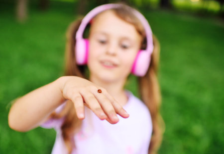 a little girl in pink headphones looks at a ladybug on her hand.の写真素材
