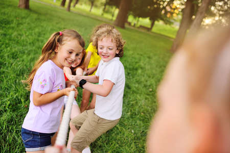 group of preschool children - boys and girls compete in a tug of war against the background of a park and greenery.の写真素材