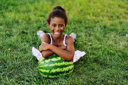 cute black African American girl lying leaning on a big watermelon in the Park on a Sunny summer dayの写真素材
