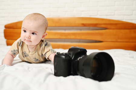 small child or baby boy on a white bed with a modern camera.の写真素材