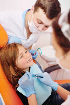 young dentists, a man and a woman, examine the teeth of a childs patient - a little pretty girl who is sitting in an orange dental chair.の写真素材
