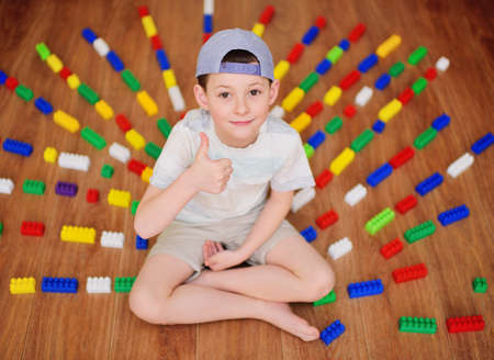 a child a small boy a preschooler in a cap worn backwards sitting on the floor shows a thumbs up-a...