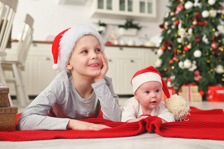 brother with little sister baby in santa hats lie and smile on the background of the christmas tree.の写真素材