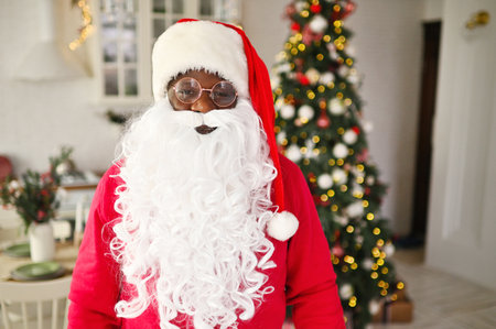 african american man in a santa costume smiles against the background of christmas decorの写真素材