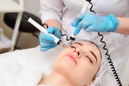 cosmetologist conducts microcurrent facial therapy for a young woman using a device in a beauty...