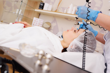 cosmetologist conducts microcurrent facial therapy for a young woman using a device in a beauty...