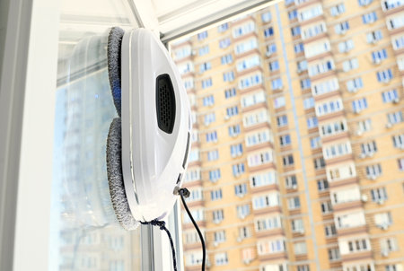 window cleaner robot cleans dirt on a window pane against the background of a multi-storey building and the sky.の写真素材