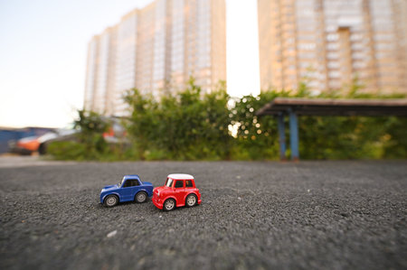 two toy cars against the backdrop of a multi-storey new building and greenery.の写真素材