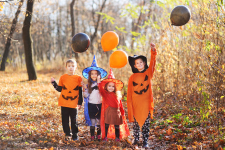 children in carnival costumes with orange and black balloons and pumpkin Jack in their hands celebrate Halloween.の写真素材