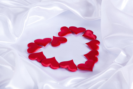 small hearts on white silk background laid out in the shape of a big heartの写真素材
