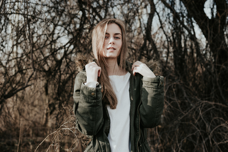 Beautiful young woman with blonde hair, wide eyebrows and blue eyes looking at camera. Girl posing at camera in green jacket. Beauty young european model in winter.の写真素材