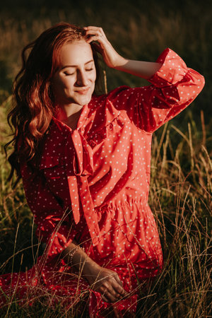 beautiful girl in a red dress and a plaid shirt in a wheat field holding her head by one armの写真素材