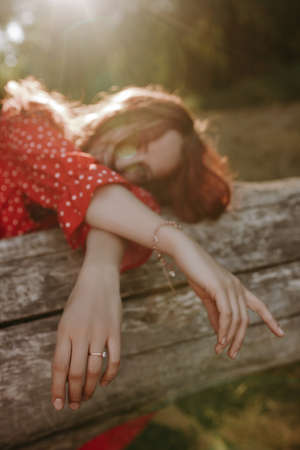 Young woman with red long curly thick hair lying down on a dry fallen tree in the middle of forest glade. Female person crossed her arms lying her head on treeの写真素材