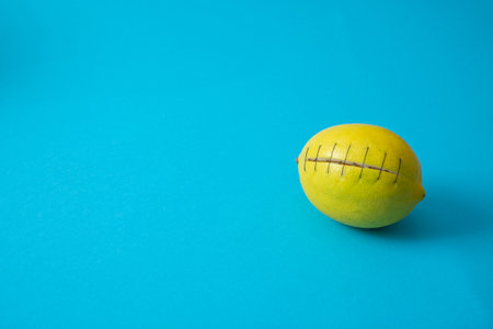 Yellow lemon fruit cut with stitches holding it. Blue background. Minimal concept.の写真素材