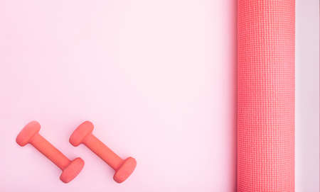 Pink feminine exercise concept with women's dumbbells, yoga mat, and copy space. Minimal artistic flat lay.の写真素材