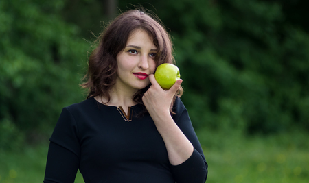 beautiful girl in a black dress holding a green apple in the forestの写真素材