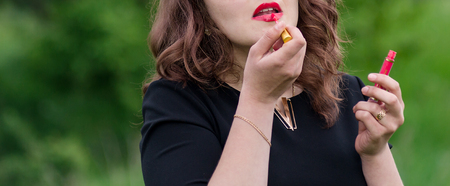 Beautiful girl with curly hair put red lipstick on the lipsの写真素材