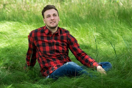 Trendy guy is smiling and  resting on the grassの写真素材