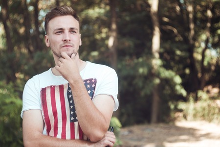 Portrait of a stylish young man in a T-shirt with an American flag. A student in the park.の写真素材