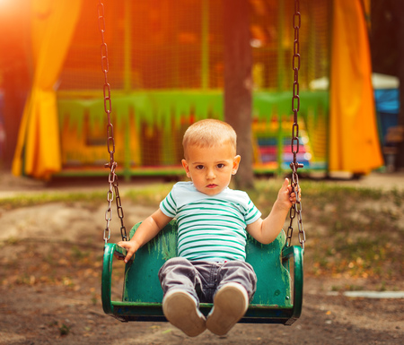 Little blonde boy having fun at the playground. Child kid playing on a swing outdoor. Happy active childhood.の写真素材