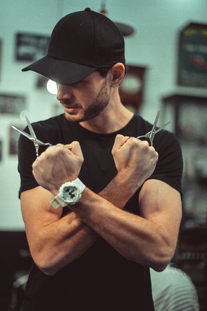 Portrait of a young bearded hairdresser in a black T-shirt with scissors in her hands.の写真素材