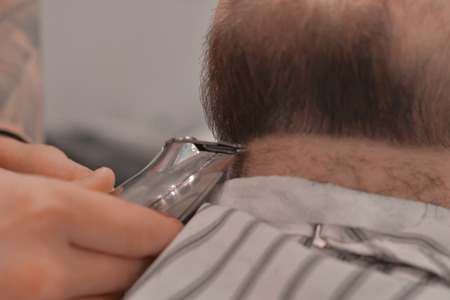 Man's hands in gloves doing a haircut for man with dark hair and beard at barber shop, close up portrait, copy space.の写真素材